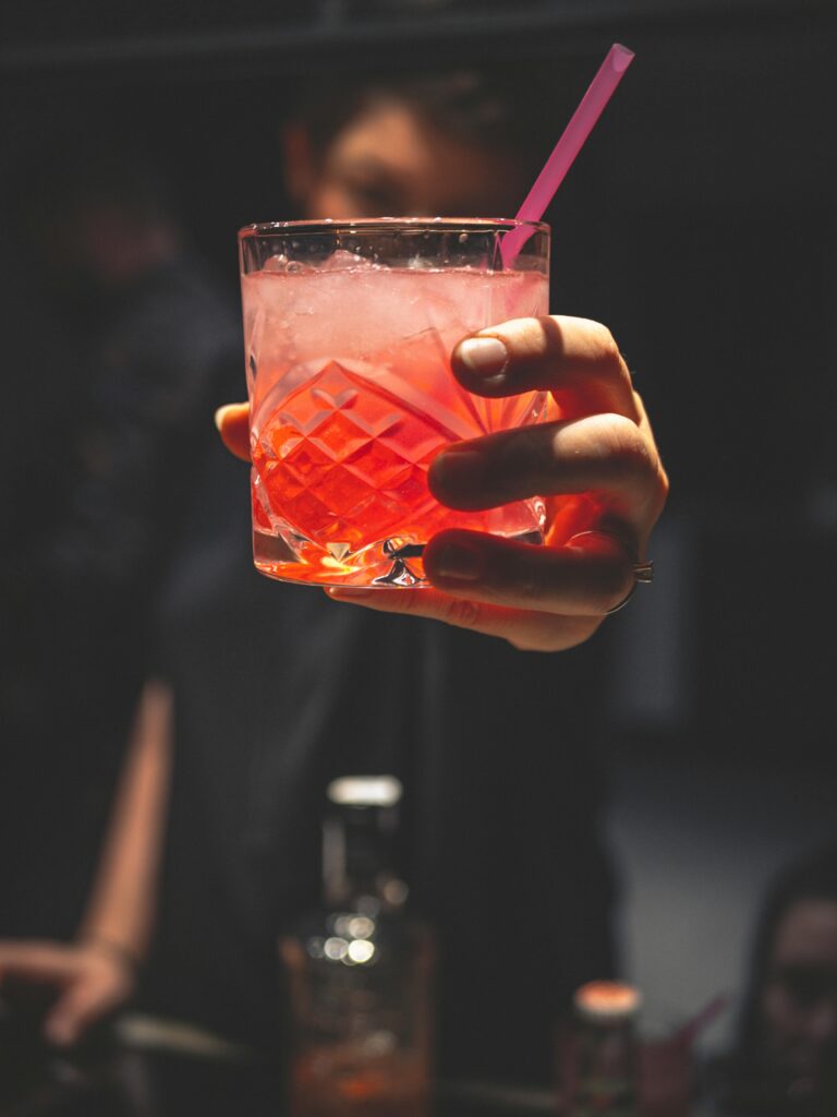 Close-up of a hand holding a vibrant cocktail with ice and a straw, perfect for nightlife themes.